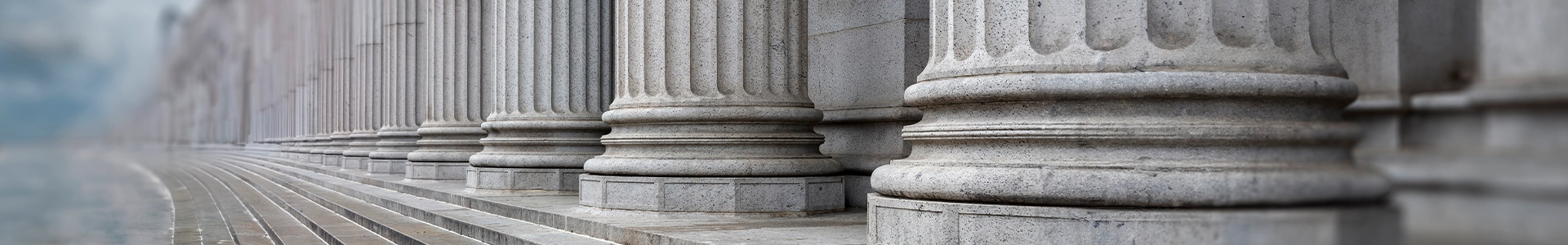 Row of large stone columns with fluted detailing at the base of a classical government or courthouse building.